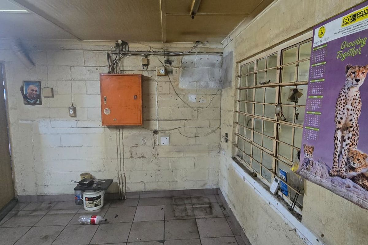 A functional utility space featuring tiled flooring, security bars on the window, and an exposed electrical distribution board, requiring maintenance and cosmetic updates.