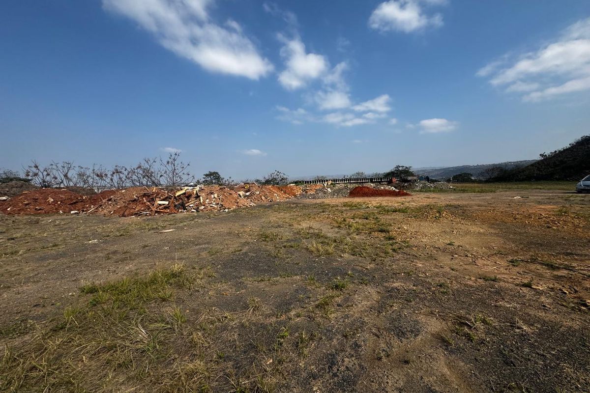 A wide-angle view of a vacant commercial land plot featuring uneven terrain and piles of debris.