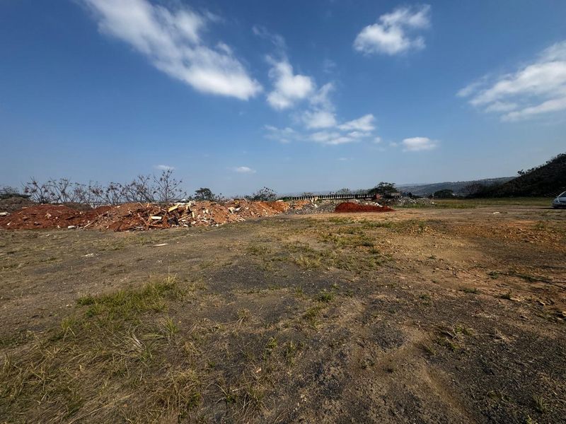 A wide-angle view of a vacant commercial land plot featuring uneven terrain and piles of debris.