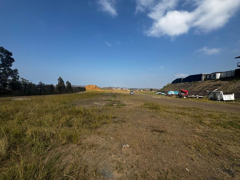 A wide-angle view of a vacant commercial land plot featuring perimeter fencing, a retaining wall, and an unimproved ground surface.