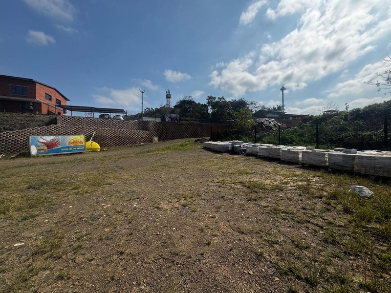 A view of a vacant commercial land plot featuring a retaining wall, perimeter fencing, and an existing billboard structure.