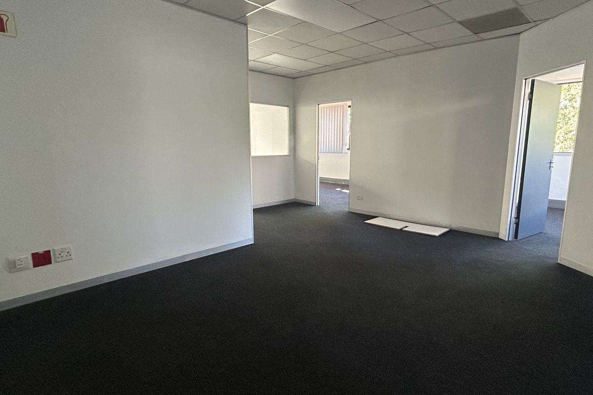 An empty, open-plan office space featuring dark carpeting, a suspended ceiling, and neutral walls, providing a versatile layout for professional use.