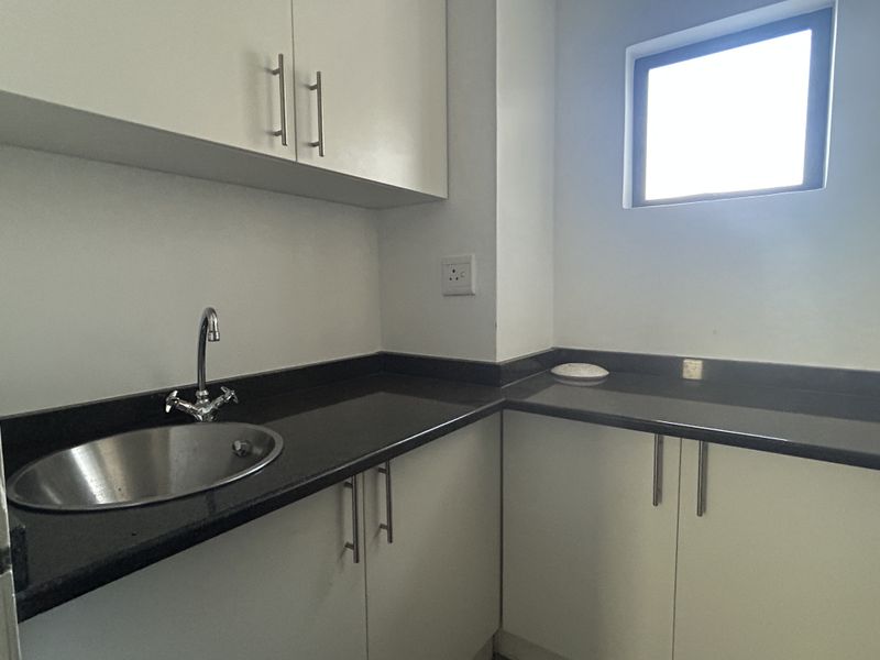 A clean and functional scullery area featuring white built-in cabinetry, dark stone countertops, and a stainless steel sink.