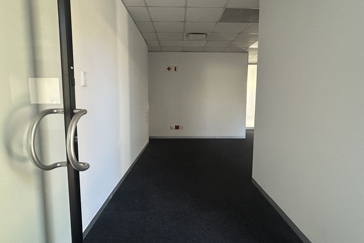 An empty office space featuring a suspended ceiling, dark carpeted flooring, and a glass entrance door.