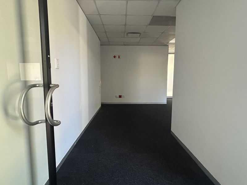 An empty office space featuring a suspended ceiling, dark carpeted flooring, and a glass entrance door.