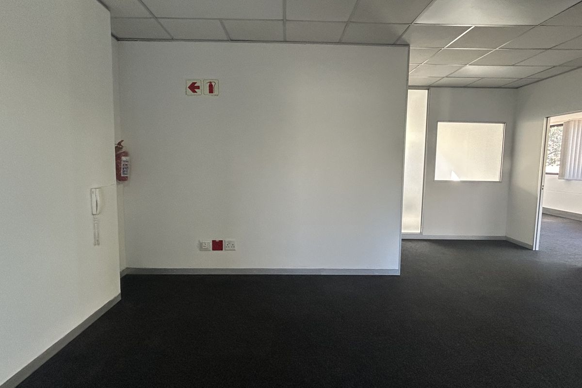 An empty office space featuring a suspended ceiling, dark carpeting, and an internal glass partition, providing a clean and functional professional environment.