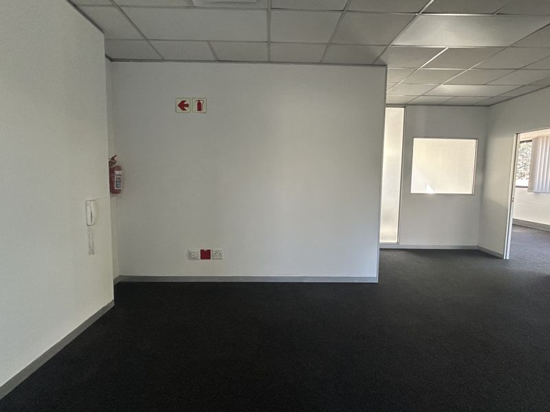 An empty office space featuring a suspended ceiling, dark carpeting, and an internal glass partition, providing a clean and functional professional environment.