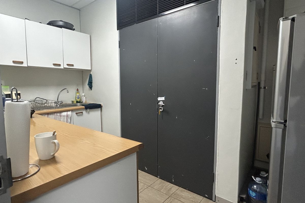 A functional office kitchenette featuring built-in cabinetry, a laminate countertop, stainless steel sink, and durable tiled flooring.