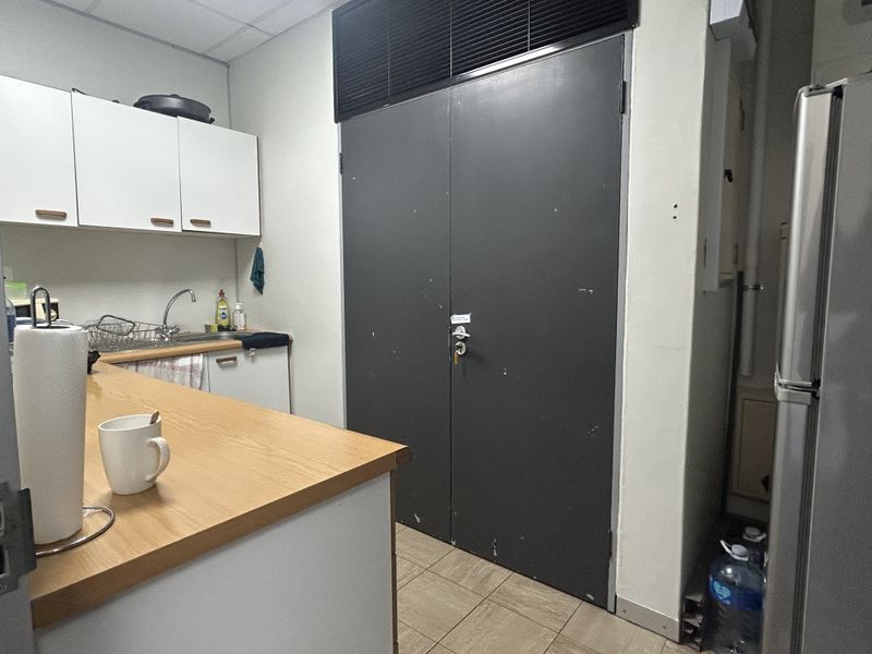 A functional office kitchenette featuring built-in cabinetry, a laminate countertop, stainless steel sink, and durable tiled flooring.