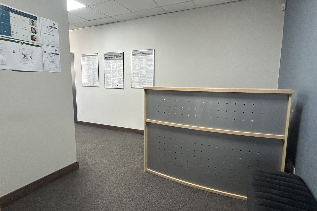 A professional office reception area featuring a built-in reception desk, suspended ceiling tiles, and carpeted flooring.