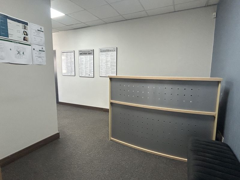 A professional office reception area featuring a built-in reception desk, suspended ceiling tiles, and carpeted flooring.