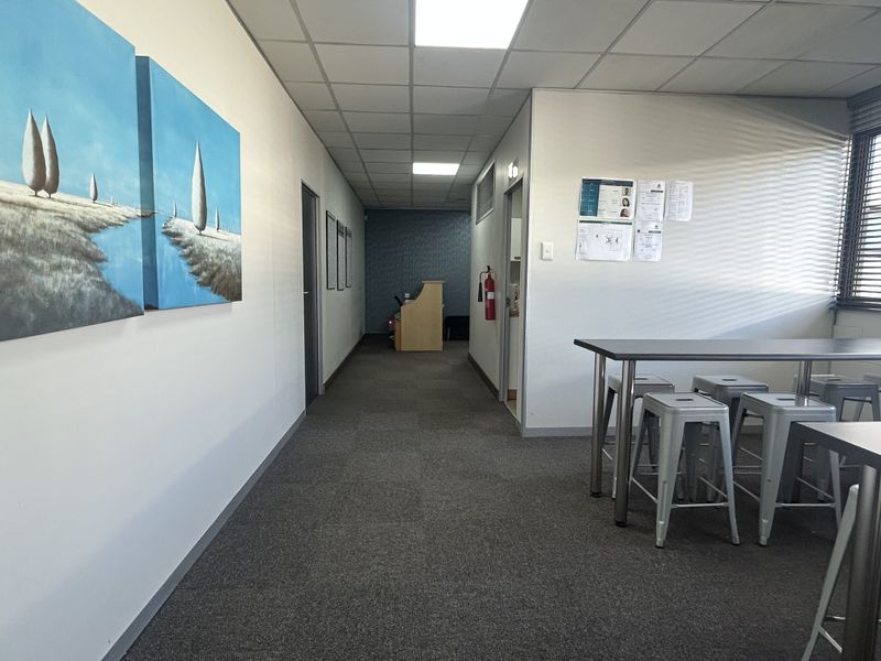 A functional office corridor and breakout area featuring carpet tiles, a suspended ceiling with recessed lighting, and window blinds.