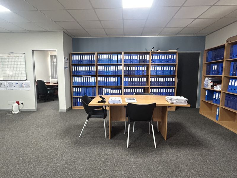 A functional office space featuring carpeted flooring, a suspended ceiling with recessed lighting, and extensive built-in shelving for organized storage.