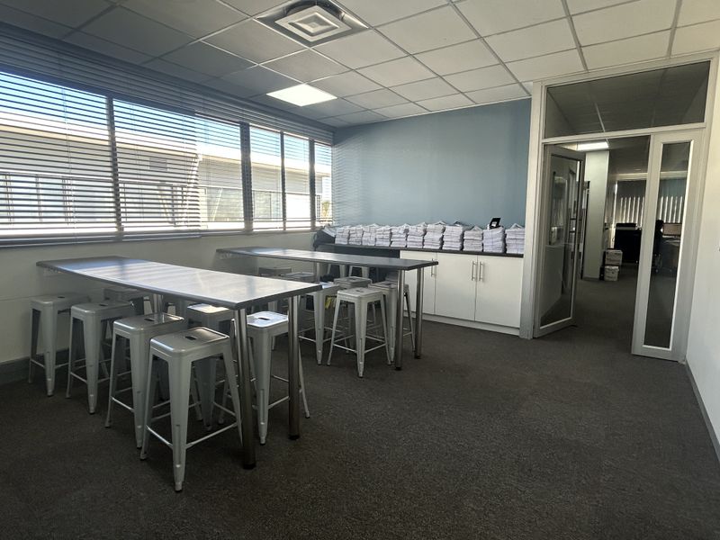 A functional office space featuring a suspended ceiling, recessed lighting, built-in storage cabinetry, and large windows with venetian blinds.