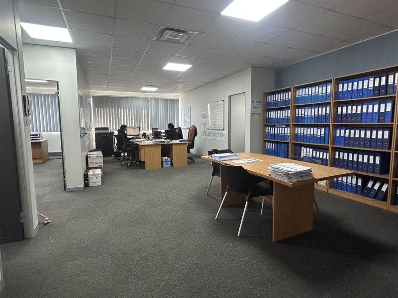 A functional office space featuring carpeted flooring, suspended ceilings with recessed lighting, and extensive built-in shelving for organized document storage.