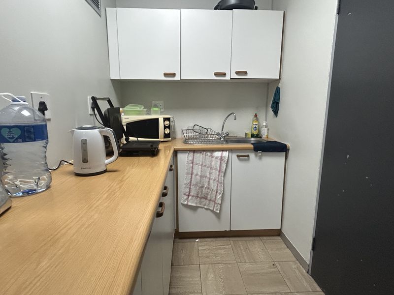 A compact office kitchenette featuring white cabinetry, a laminate countertop, and a stainless steel sink, providing essential utility for a workspace.