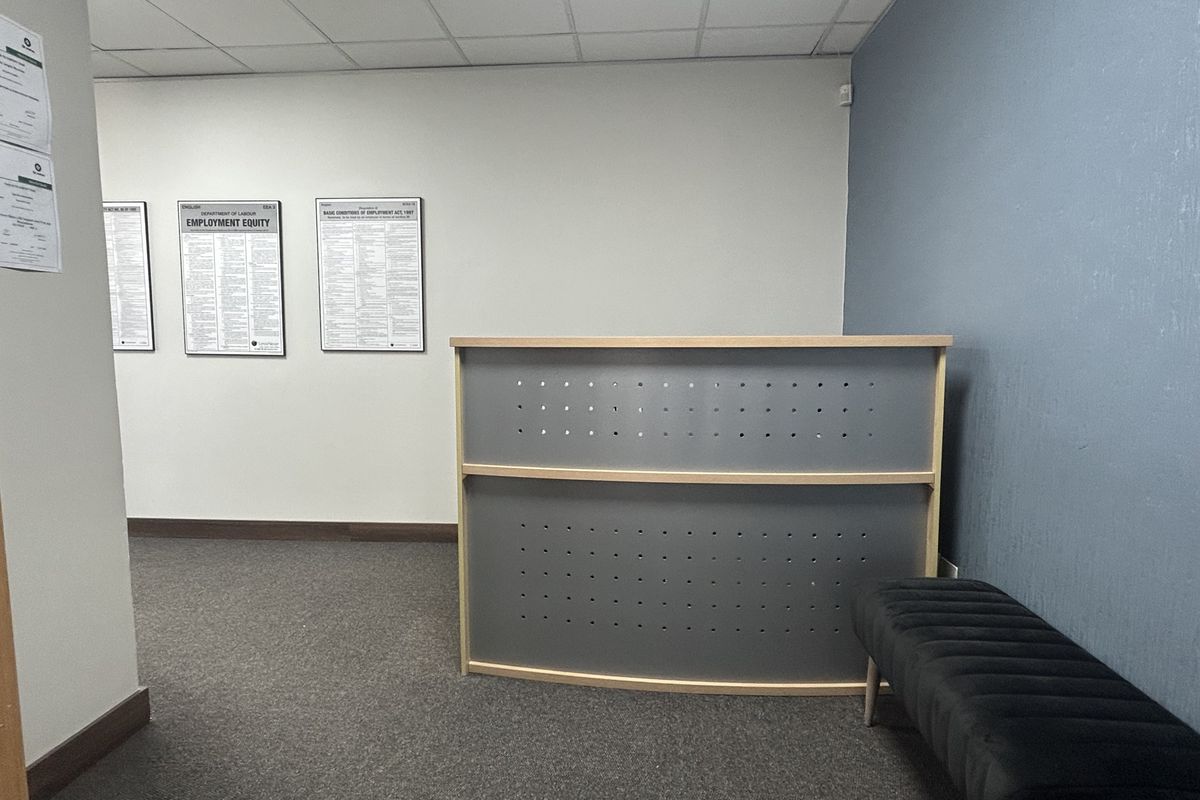 A professional office reception area featuring a modern desk, carpeted flooring, and a suspended ceiling, providing a clean and functional workspace environment.