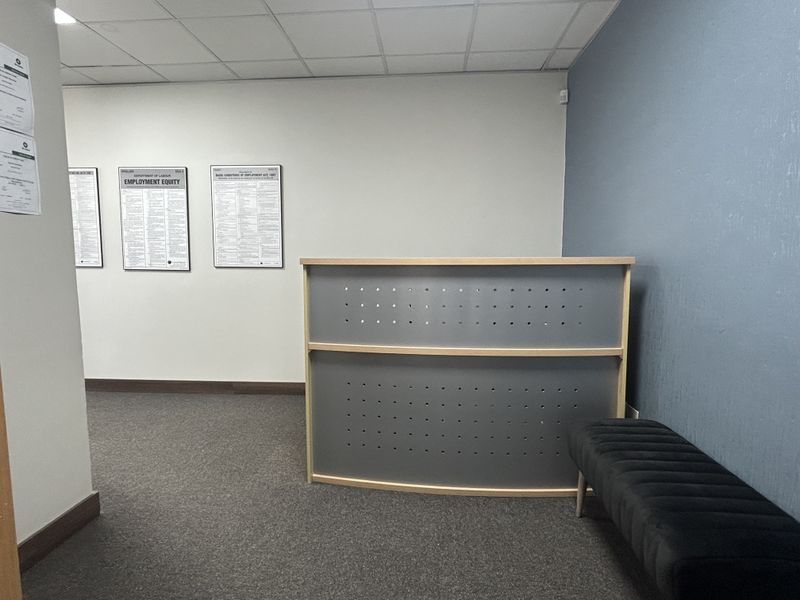 A professional office reception area featuring a modern desk, carpeted flooring, and a suspended ceiling, providing a clean and functional workspace environment.