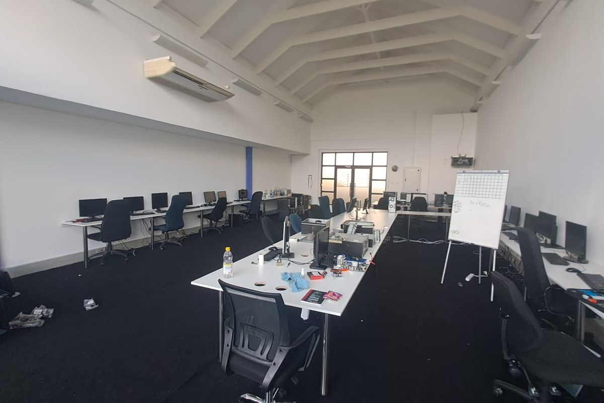 Spacious open-plan office area featuring high vaulted ceilings with exposed rafters, wall-mounted air conditioning, and large windows providing natural light.