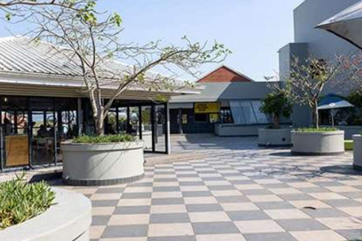 A spacious outdoor patio area featuring checkered paving, built-in concrete planters, and a modern office building facade with large glass windows.