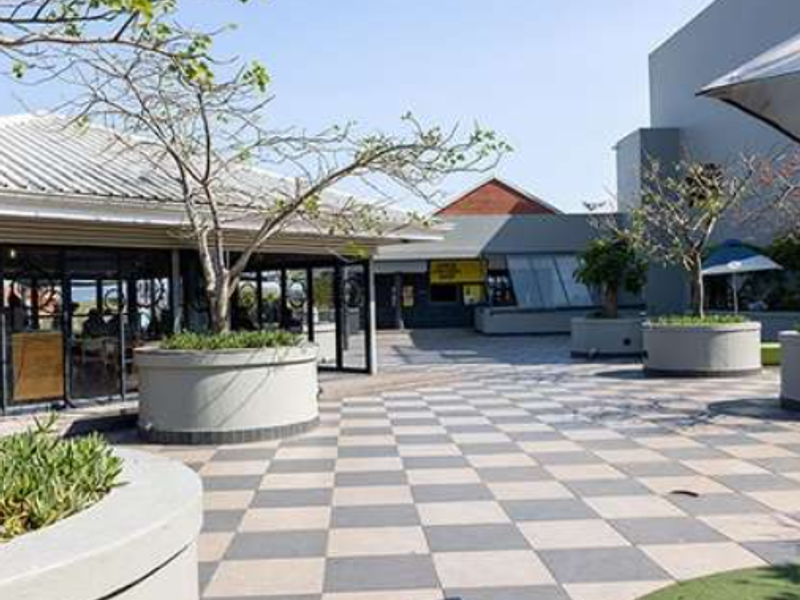 A spacious outdoor patio area featuring checkered paving, built-in concrete planters, and a modern office building facade with large glass windows.