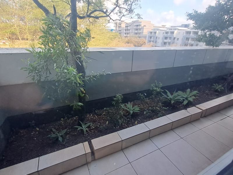 A private balcony featuring tiled flooring and a built-in planter bed, offering an outdoor space with views of the surrounding office complex.