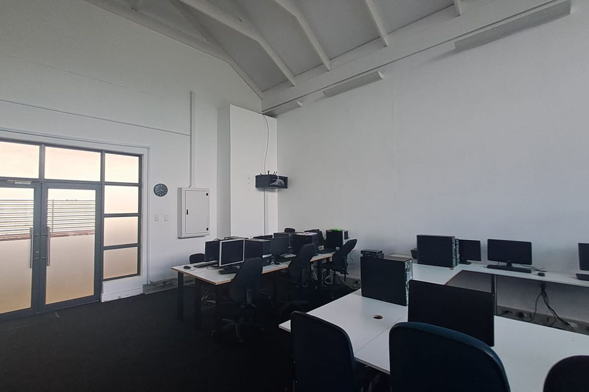 Spacious office area featuring high vaulted ceilings with exposed trusses, carpeted flooring, and direct access to an outdoor balcony through a glass door.