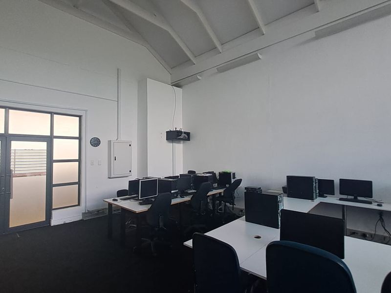 Spacious office area featuring high vaulted ceilings with exposed trusses, carpeted flooring, and direct access to an outdoor balcony through a glass door.