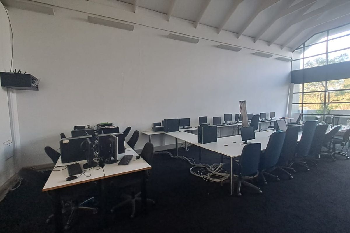 Spacious office area featuring a high vaulted ceiling, large windows providing natural light, and carpeted flooring, suitable for a collaborative workspace.
