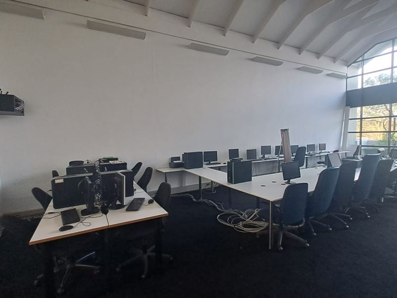 Spacious office area featuring a high vaulted ceiling, large windows providing natural light, and carpeted flooring, suitable for a collaborative workspace.
