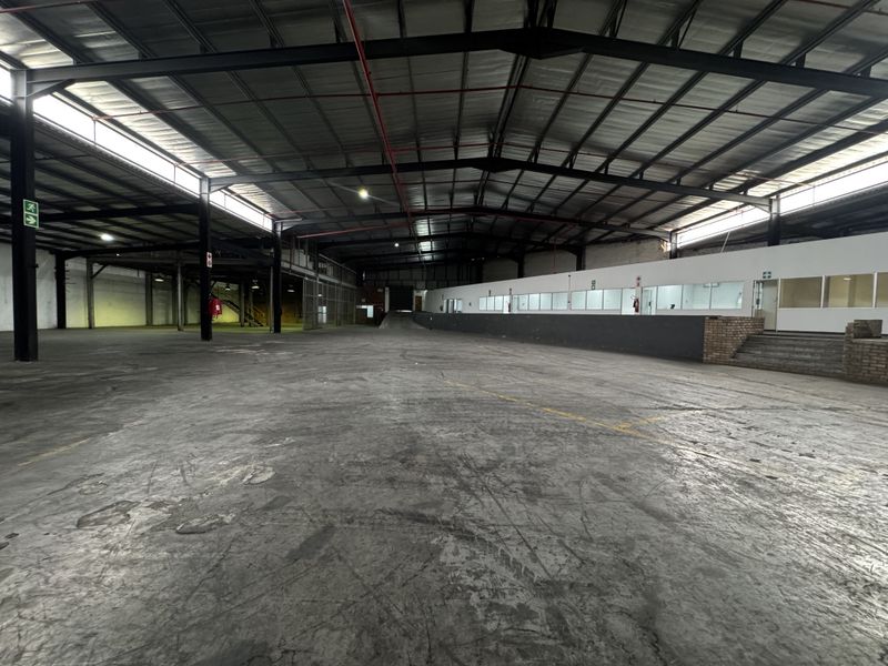 Spacious industrial warehouse featuring an exposed steel portal frame, concrete flooring, fire sprinkler system, and an integrated internal office partition.