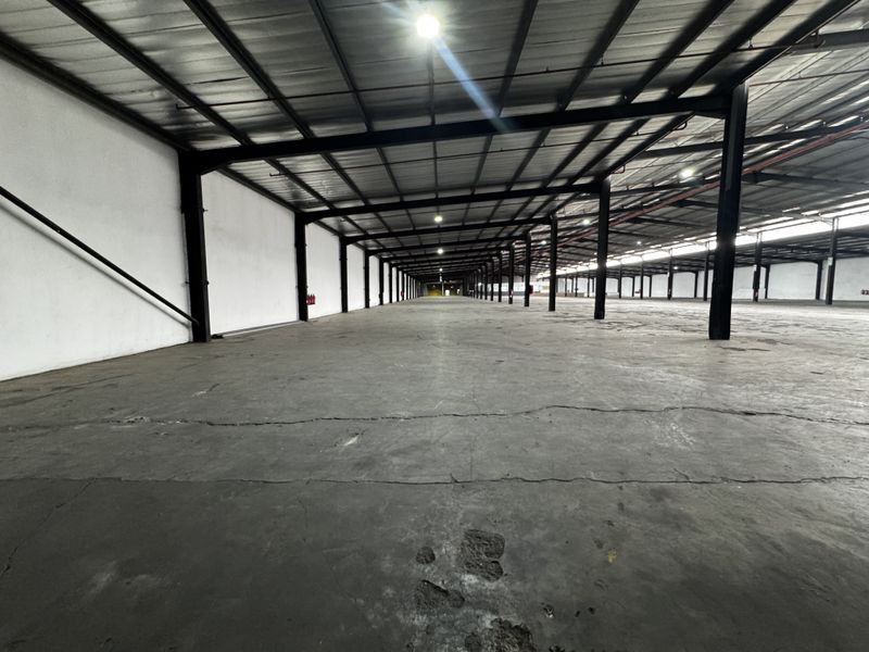 Expansive industrial warehouse space featuring a high-clearance steel portal frame structure, concrete flooring, and metal roof sheeting, suitable for storage or manufacturing operations.
