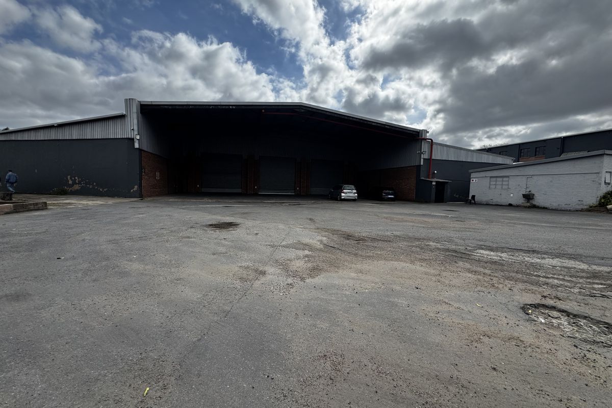 Industrial warehouse facility featuring a large asphalt yard, multiple roller shutter doors, and metal cladding exterior.