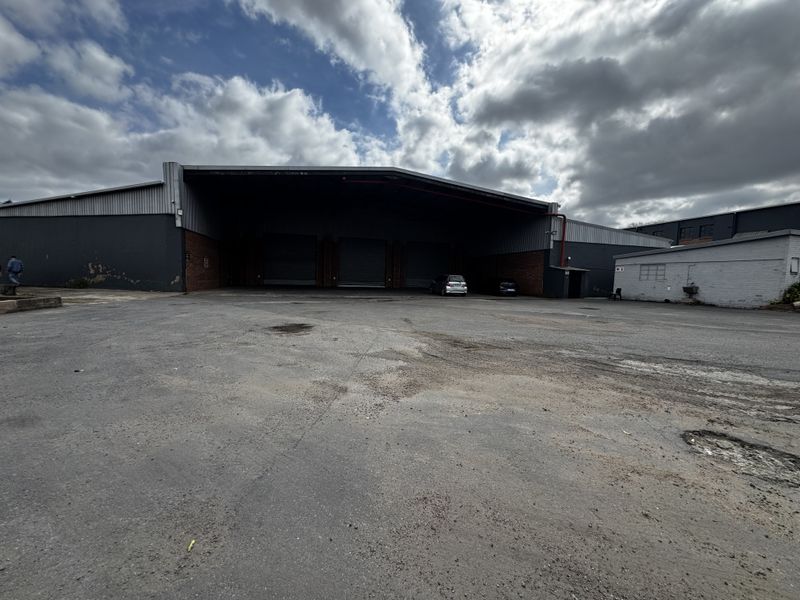 Industrial warehouse facility featuring a large asphalt yard, multiple roller shutter doors, and metal cladding exterior.