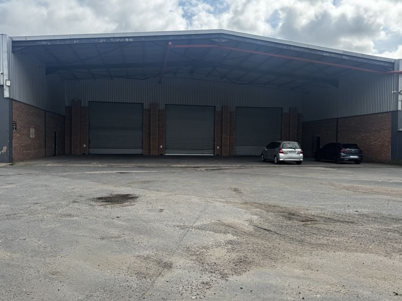 Industrial warehouse facility featuring three large roller shutter doors, steel frame construction, and a spacious asphalt yard area.