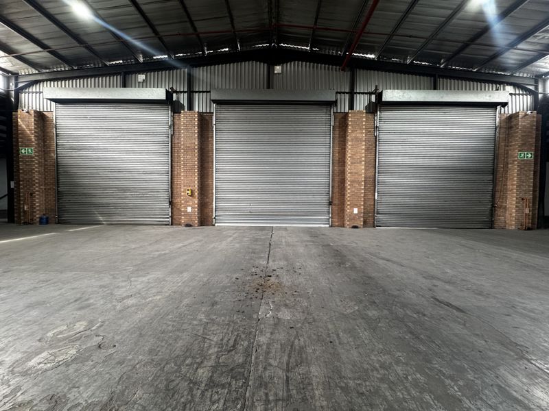 Spacious industrial warehouse interior featuring three large roller shutter doors, exposed steel roof structure, and durable concrete flooring.