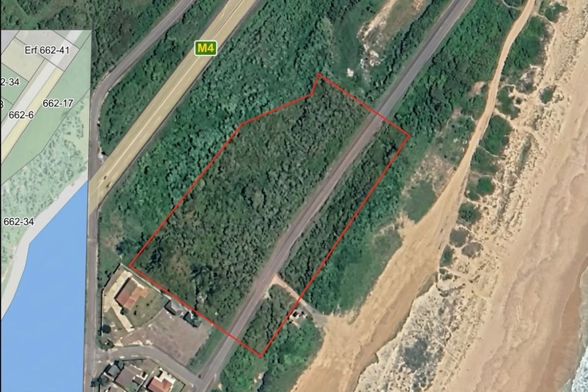 Aerial view of a vacant commercial land parcel situated near the coastline, featuring natural vegetation and proximity to major road infrastructure.