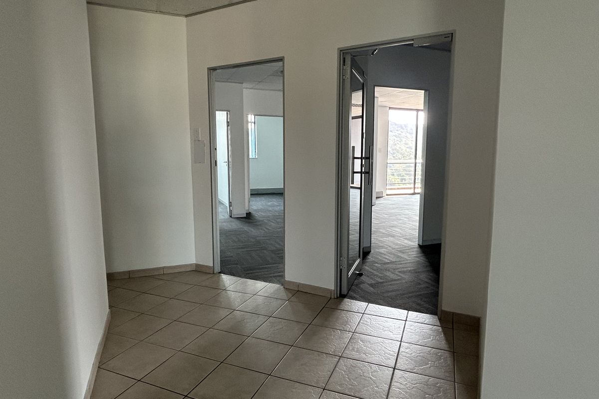 A bright office hallway featuring tiled flooring, leading into multiple vacant office spaces with carpeted floors and natural light.
