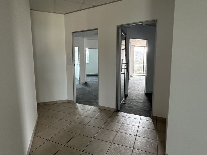 A bright office hallway featuring tiled flooring, leading into multiple vacant office spaces with carpeted floors and natural light.