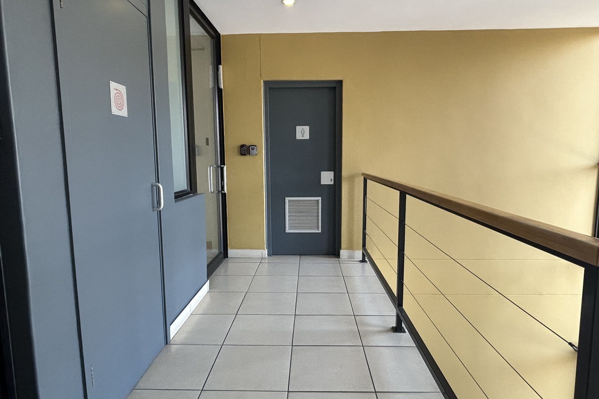 A clean, well-maintained office hallway featuring tiled flooring, a modern metal balustrade with a wooden handrail, and secure access doors.