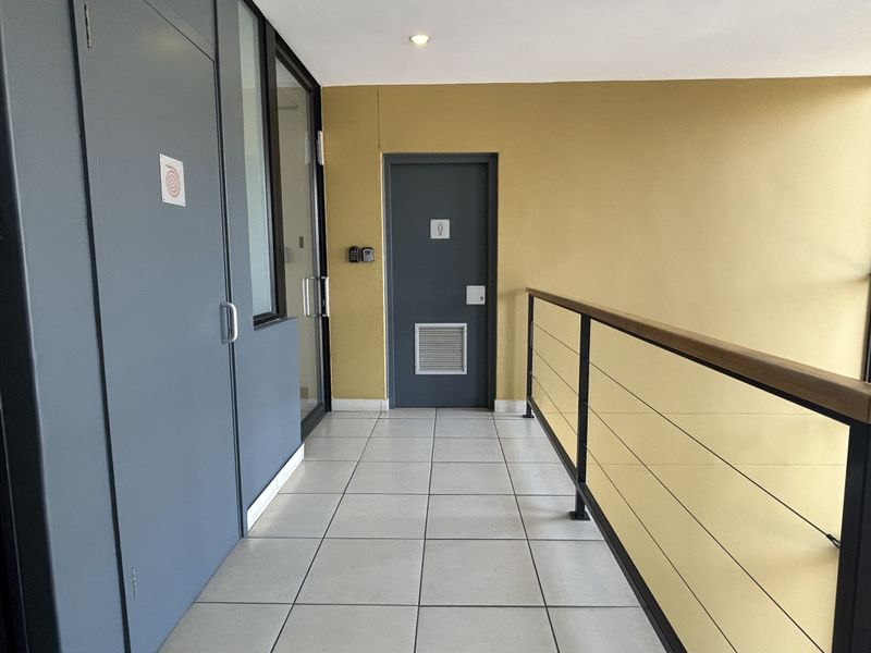A clean, well-maintained office hallway featuring tiled flooring, a modern metal balustrade with a wooden handrail, and secure access doors.