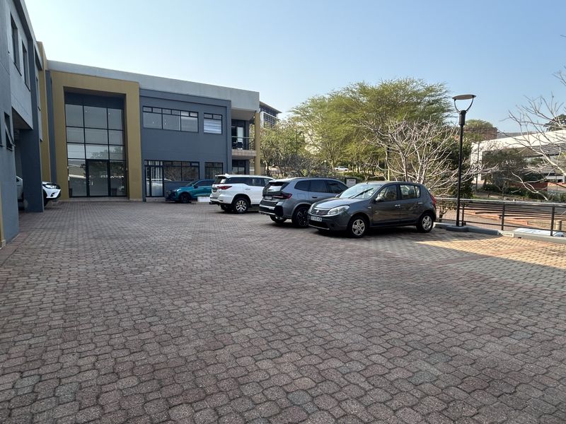 Exterior view of a modern office building featuring a paved parking area and a prominent glass facade entrance.