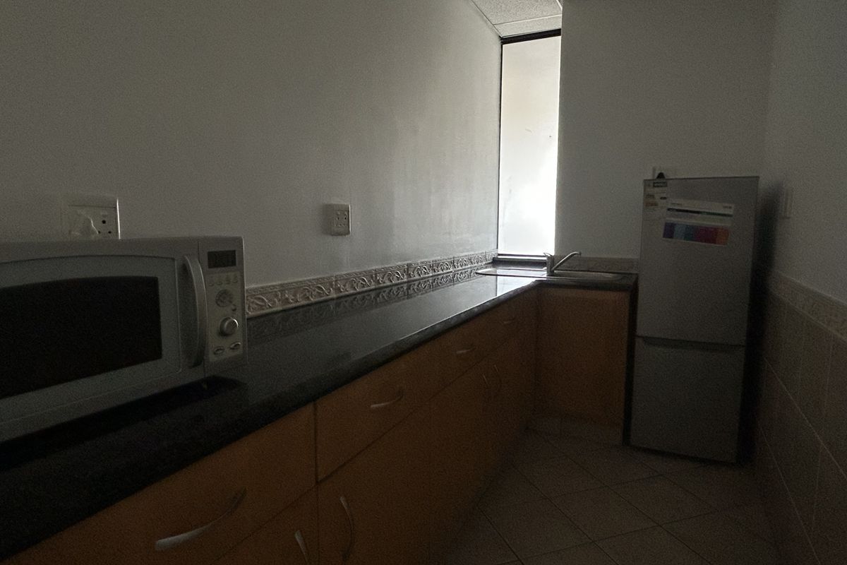 A functional office kitchenette featuring built-in wooden cabinetry, granite countertops, a stainless steel sink, and tiled flooring.