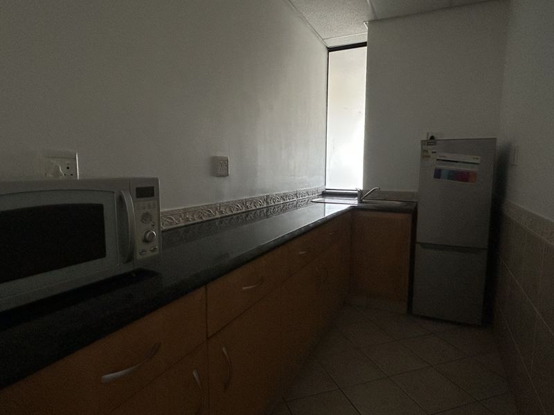 A functional office kitchenette featuring built-in wooden cabinetry, granite countertops, a stainless steel sink, and tiled flooring.