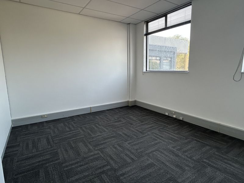 A clean, empty office space featuring dark carpet tiles, a suspended ceiling, and integrated skirting trunking for electrical and data connectivity.