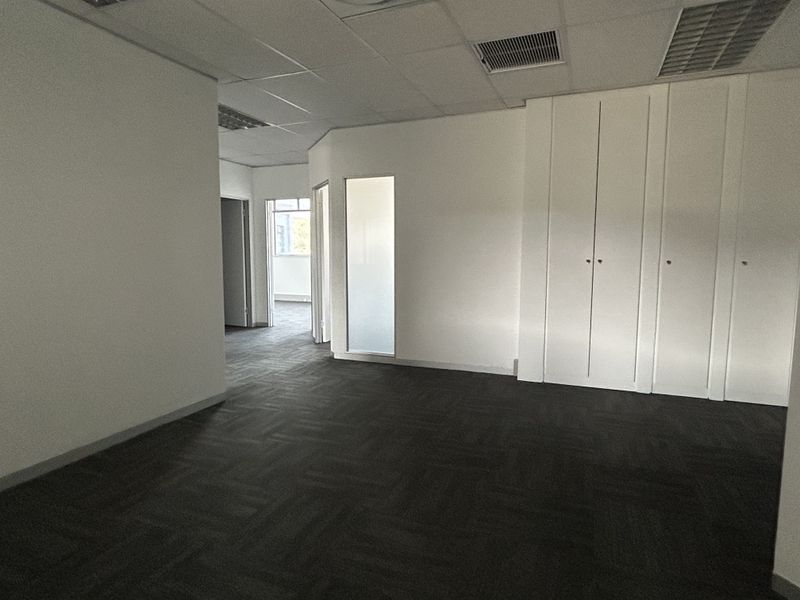 A vacant office space featuring neutral carpet tiles, a suspended ceiling with recessed lighting, and integrated floor-to-ceiling storage cupboards.