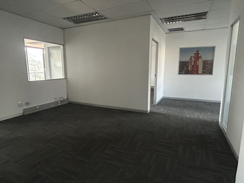 A vacant office space featuring carpet tiles, suspended ceilings with recessed lighting, and an internal glass partition, offering a clean and professional work environment.