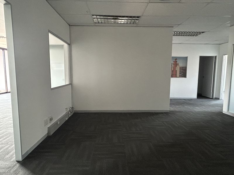 An empty office space featuring carpet tiles, suspended ceilings with recessed lighting, and an internal glass partition wall.