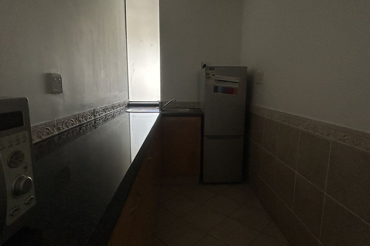 A compact kitchen area featuring granite countertops, a stainless steel sink, tiled backsplash, and built-in cabinetry with tiled flooring.