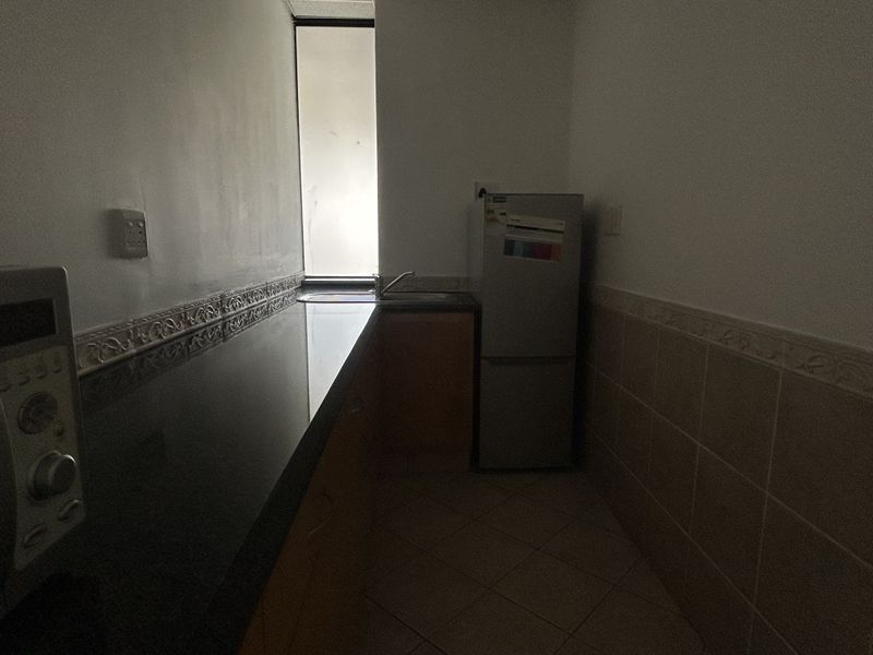 A compact kitchen area featuring granite countertops, a stainless steel sink, tiled backsplash, and built-in cabinetry with tiled flooring.